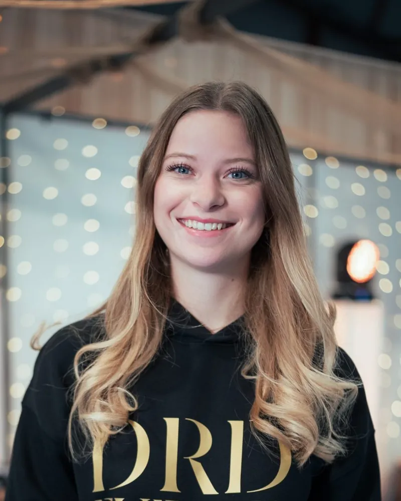 Manon souriante en sweat DRD Events devant un rideau lumineux