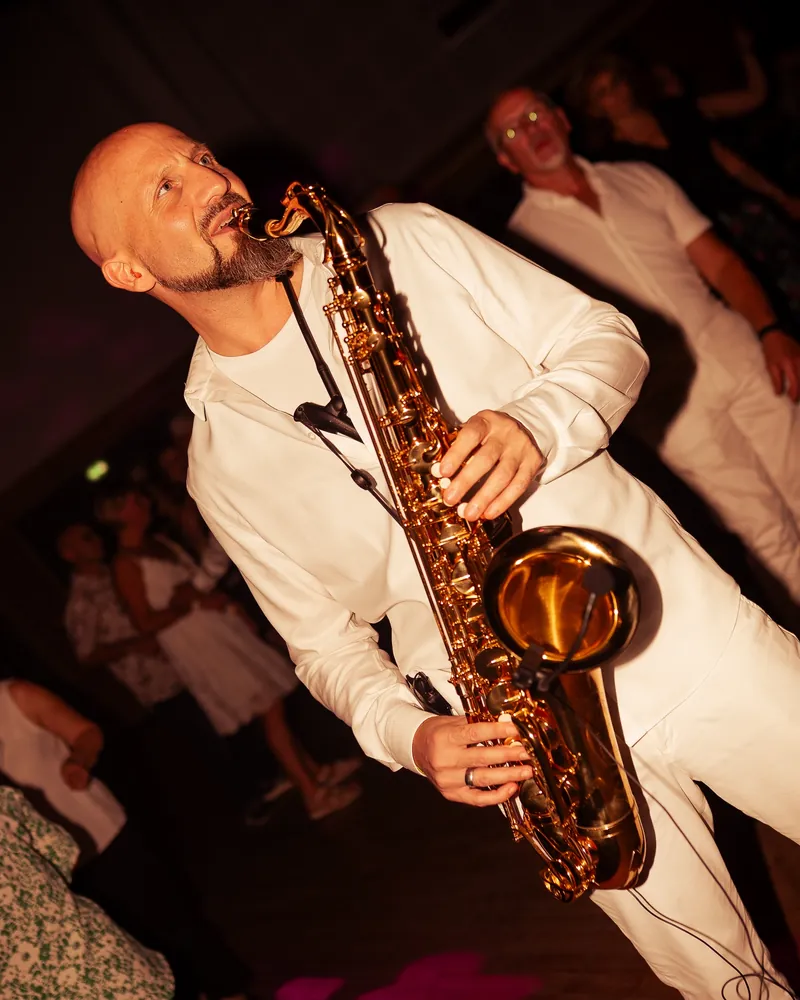 Cédric jouant du saxophone en costume blanc sur la piste de danse